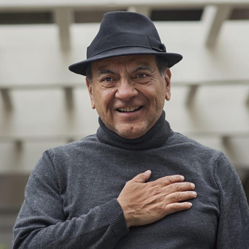 Portrait de Don Miguel Ruiz, auteur spirituel mexicain, avec une pile de ses ouvrages sur la sagesse toltèque.