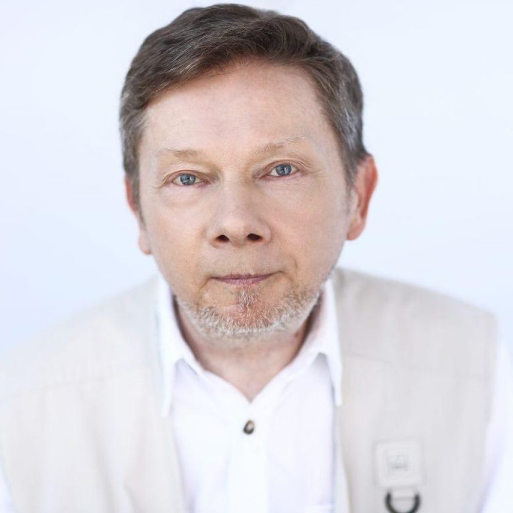 Portrait d’Eckhart Tolle, auteur spirituel renommé, assis paisiblement, les mains jointes, incarnant la sérénité et la pleine conscience.