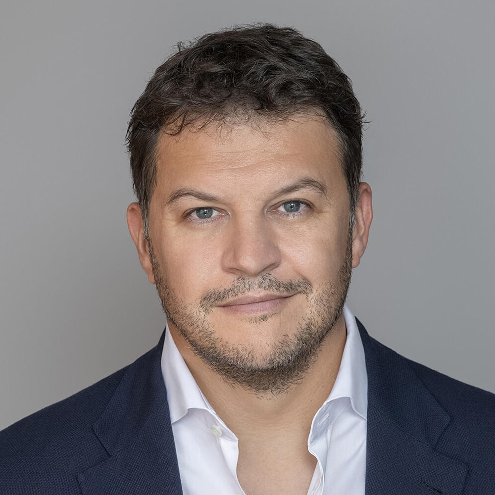 Photo de Guillaume Musso, auteur français à succès, posant devant une pile de ses romans traduits dans plusieurs langues.