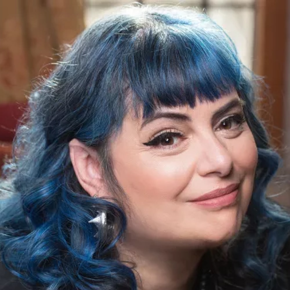 Portrait de Holly Black, autrice américaine de fantasy, devant une étagère remplie de livres féeriques.