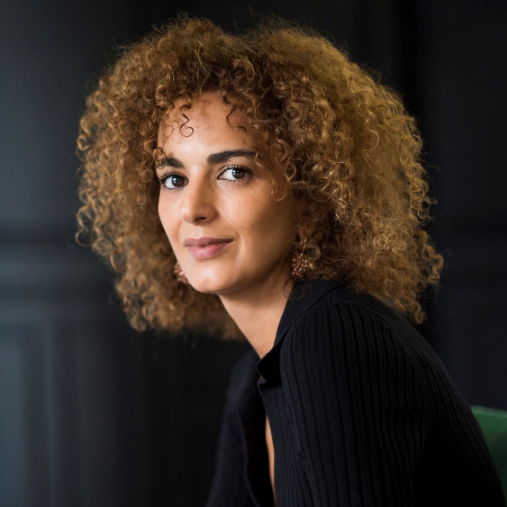 Portrait de Leïla Slimani, autrice franco-marocaine primée, posant devant une pile de ses romans engagés et intimes.