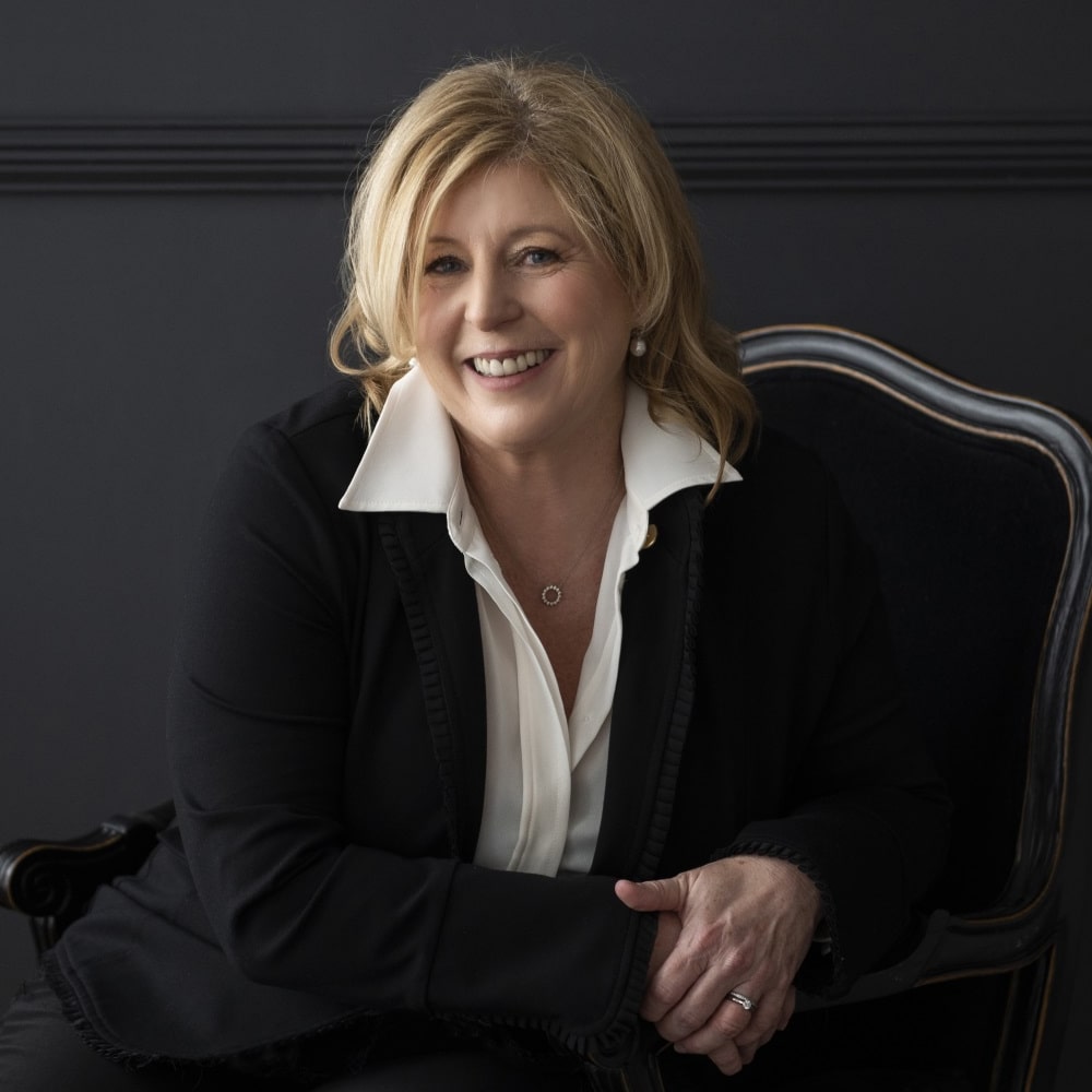 Photo de Liane Moriarty, écrivaine australienne, souriante devant une pile de ses thrillers domestiques et romans psychologiques.