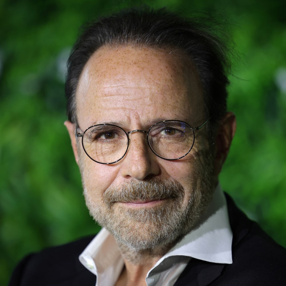 Photo de Marc Levy, écrivain français mondialement connu, posant devant une pile de ses romans mêlant amour et aventure.