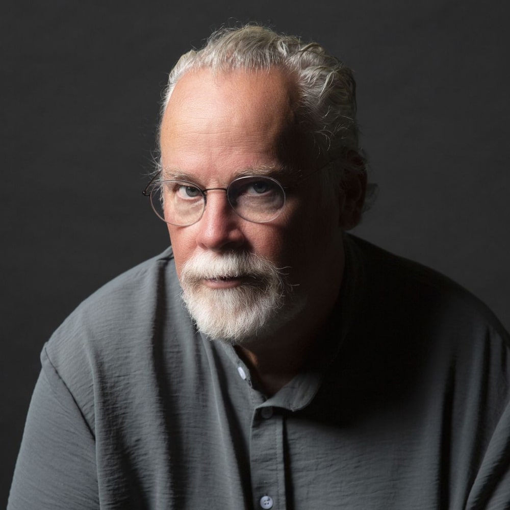 Portrait de Michael Connelly, maître du thriller américain, posant devant une pile de ses romans mettant en scène Harry Bosch.