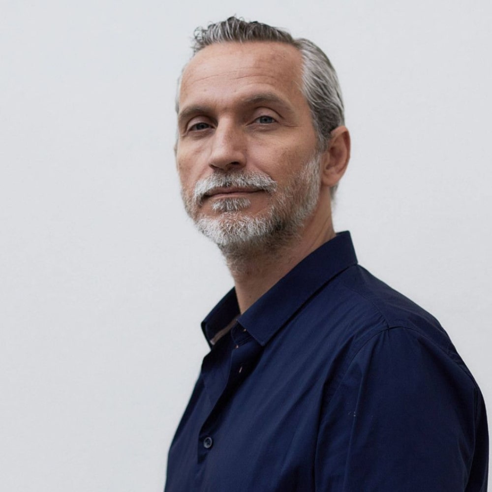 Portrait d’Olivier Norek, auteur de polars et ancien officier de police, debout devant une pile de ses thrillers réalistes.