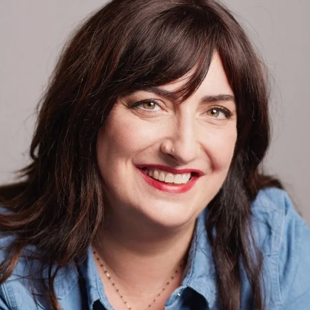Photo de Virginie Grimaldi, autrice française de romans feel-good, posant joyeusement devant une pile de ses ouvrages réconfortants.