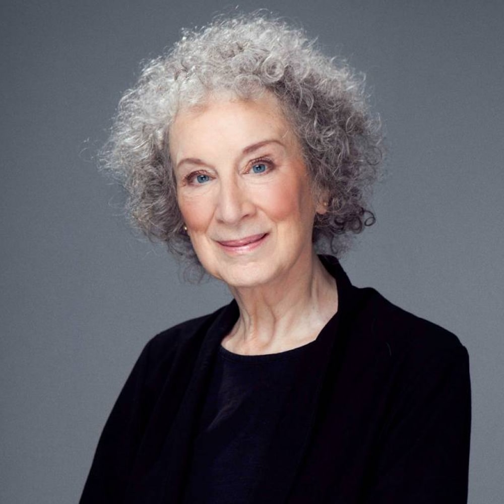 Portrait de Margaret Atwood, autrice canadienne, posant avec élégance devant une bibliothèque remplie de ses romans.
