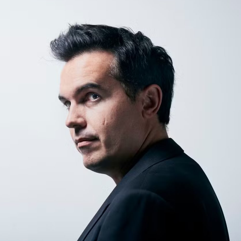 Portrait de Maxime Chattam, auteur de thrillers français, devant une bibliothèque remplie de romans.